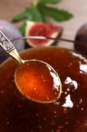 Photo of Glass bowl with tasty fig jam and spoon on table, closeup
