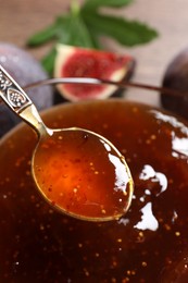 Glass bowl with tasty fig jam and spoon on table, closeup