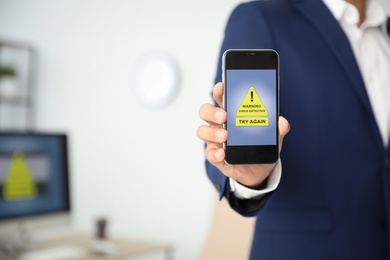 Photo of Man holding smartphone with warning about virus attack in office, closeup. Space for text