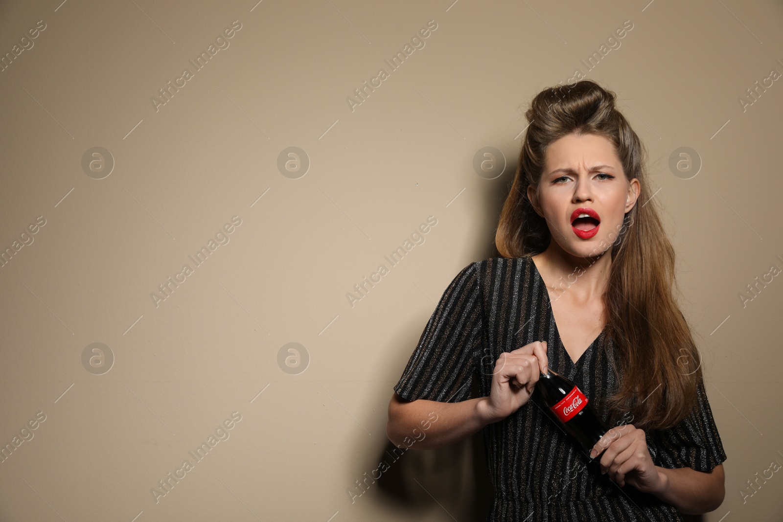 Photo of MYKOLAIV, UKRAINE - NOVEMBER 28, 2018: Young woman with bottle of Coca-Cola on color background, space for text