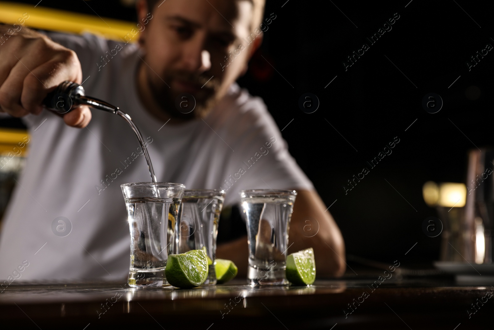 Photo of Bartender pouring Mexican Tequila into shot glass at bar counter, closeup. Space for text