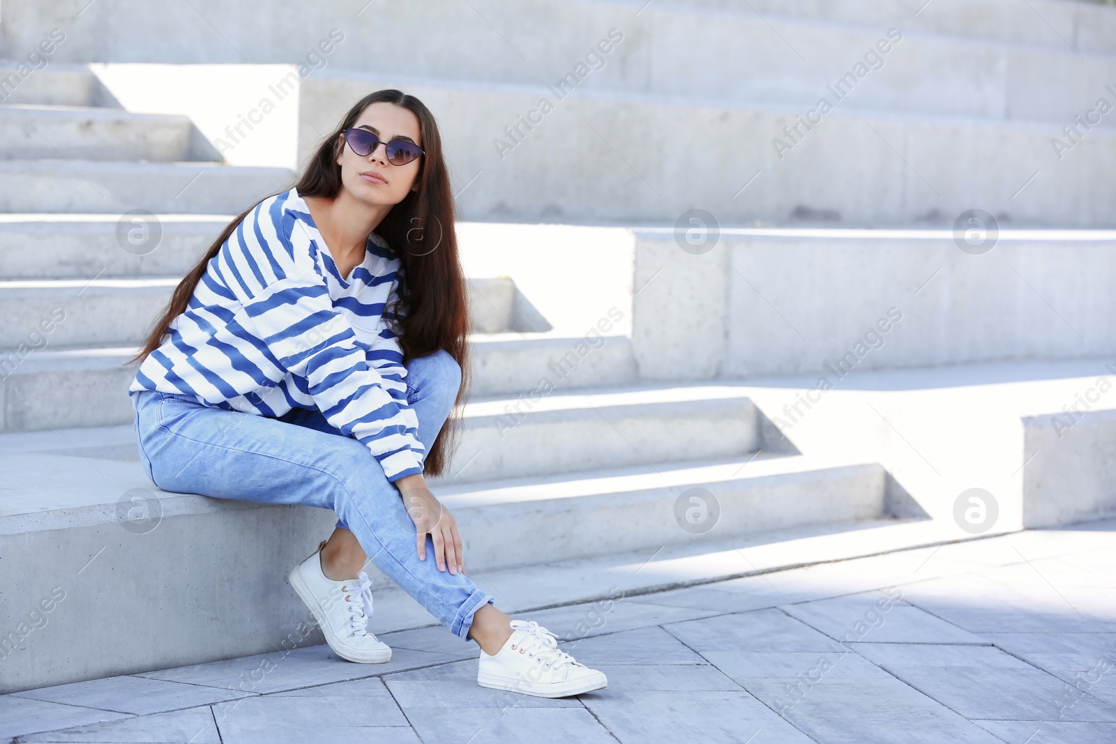 Photo of Young hipster woman in stylish jeans sitting on stairs outdoors