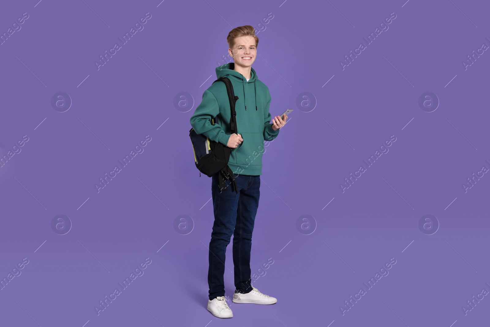 Photo of Teenage boy with backpack using smartphone on purple background