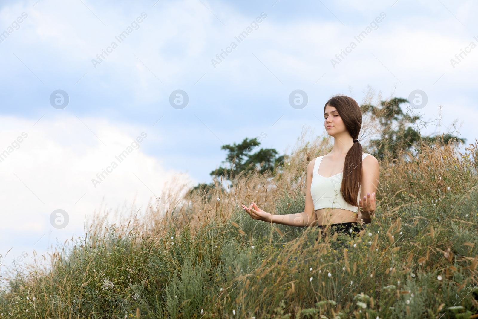 Photo of Teenage girl meditating on hill. Space for text