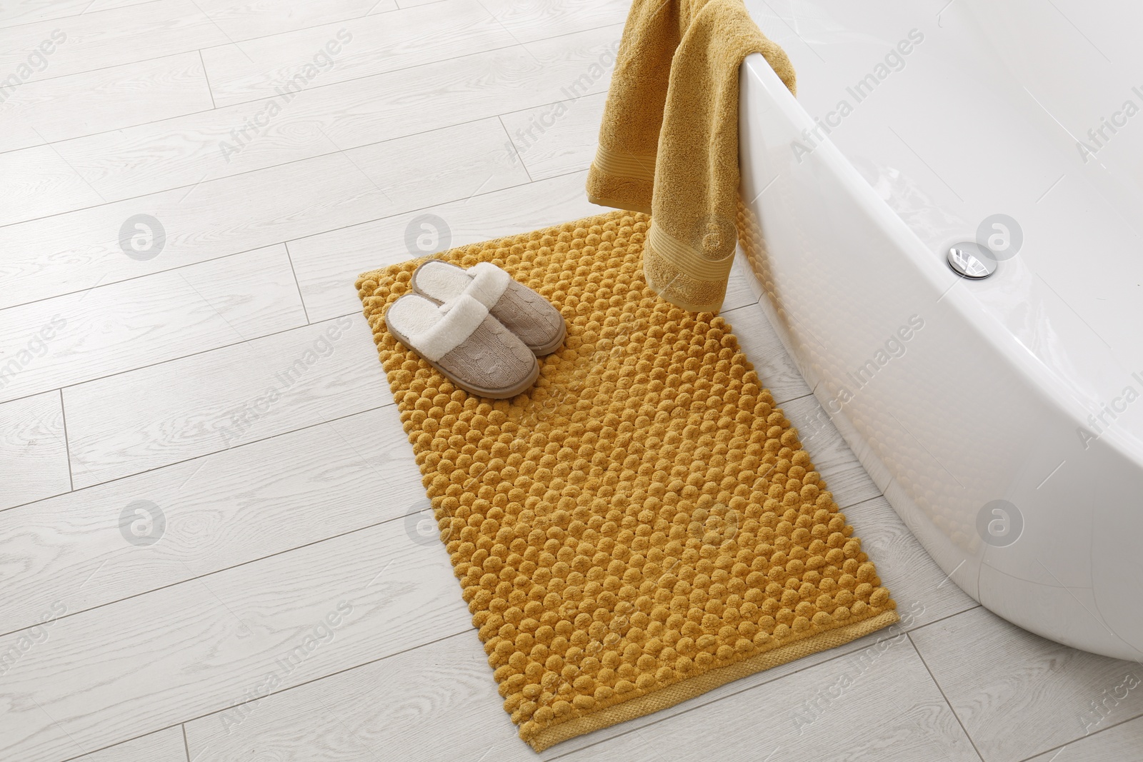 Photo of Soft orange bath mat and slippers on floor in bathroom