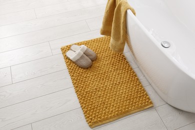 Photo of Soft orange bath mat and slippers on floor in bathroom