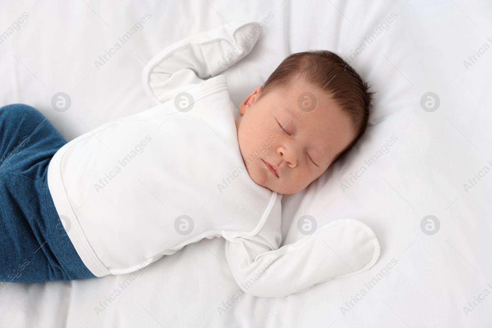 Photo of Cute newborn baby sleeping on white soft bed, top view