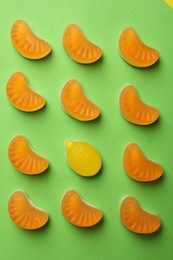 Delicious gummy orange and lemon candies on green background, flat lay