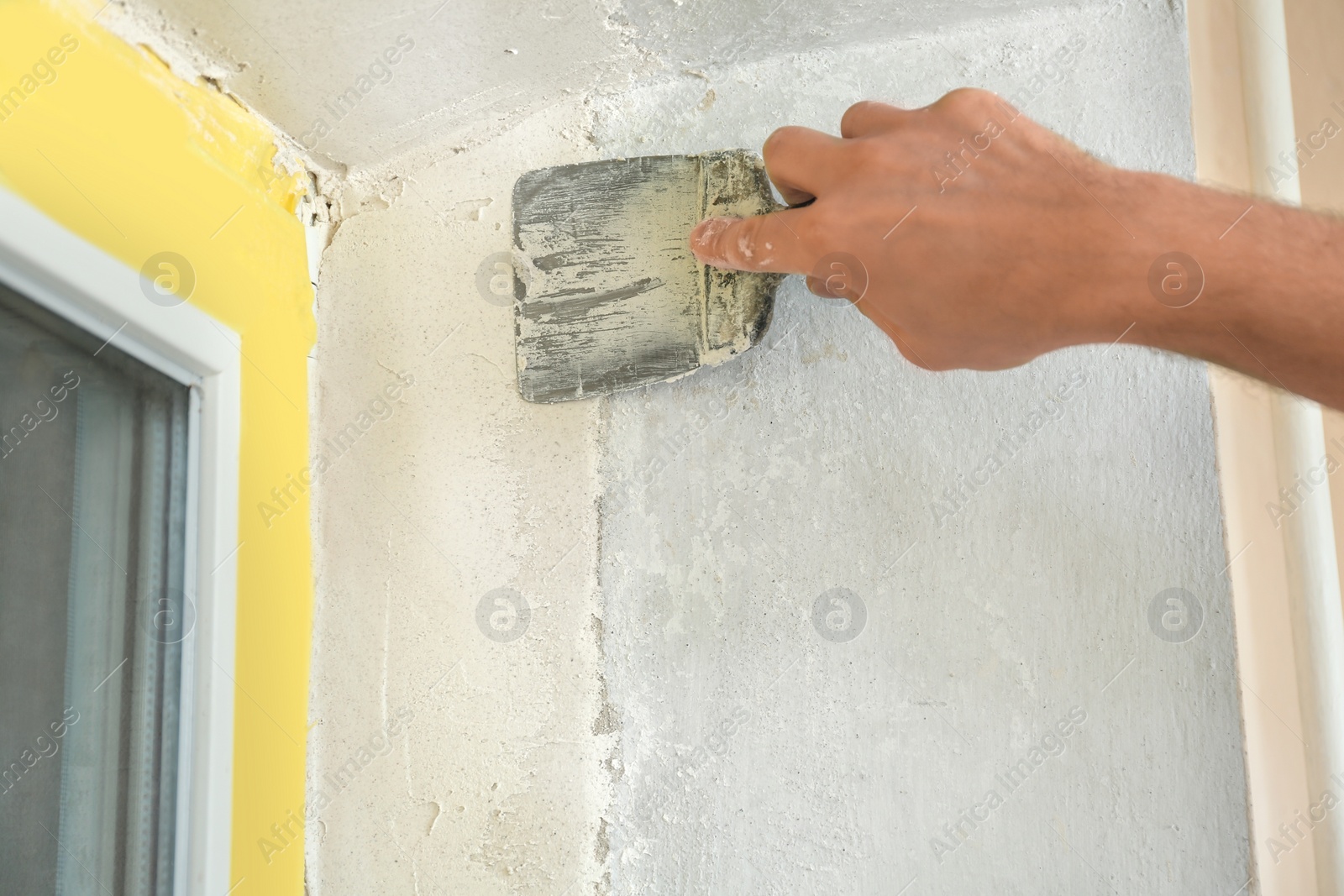 Photo of Man plastering window area with putty knife indoors, closeup. Interior repair