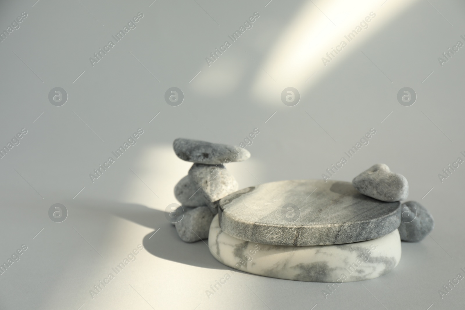 Photo of Presentation for product. Stone podium and pebbles on light grey background. Space for text