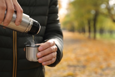 Photo of Man pouring drink from thermos into cap outdoors, closeup. Space for text
