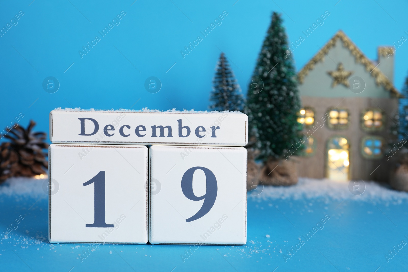 Photo of Wooden block calendar with date 19th of December and festive decor on light blue background, space for text. Saint Nicholas Day