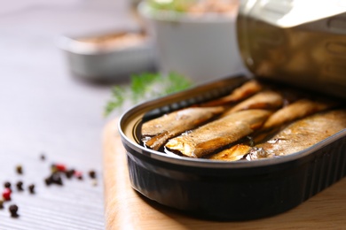 Board with tin can of sprats on wooden table, closeup. Space for text