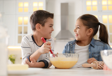 Photo of Cute little children cooking dough together in kitchen