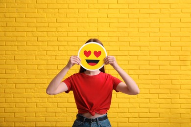 Photo of Woman covering face with heart eyes emoji near yellow brick wall