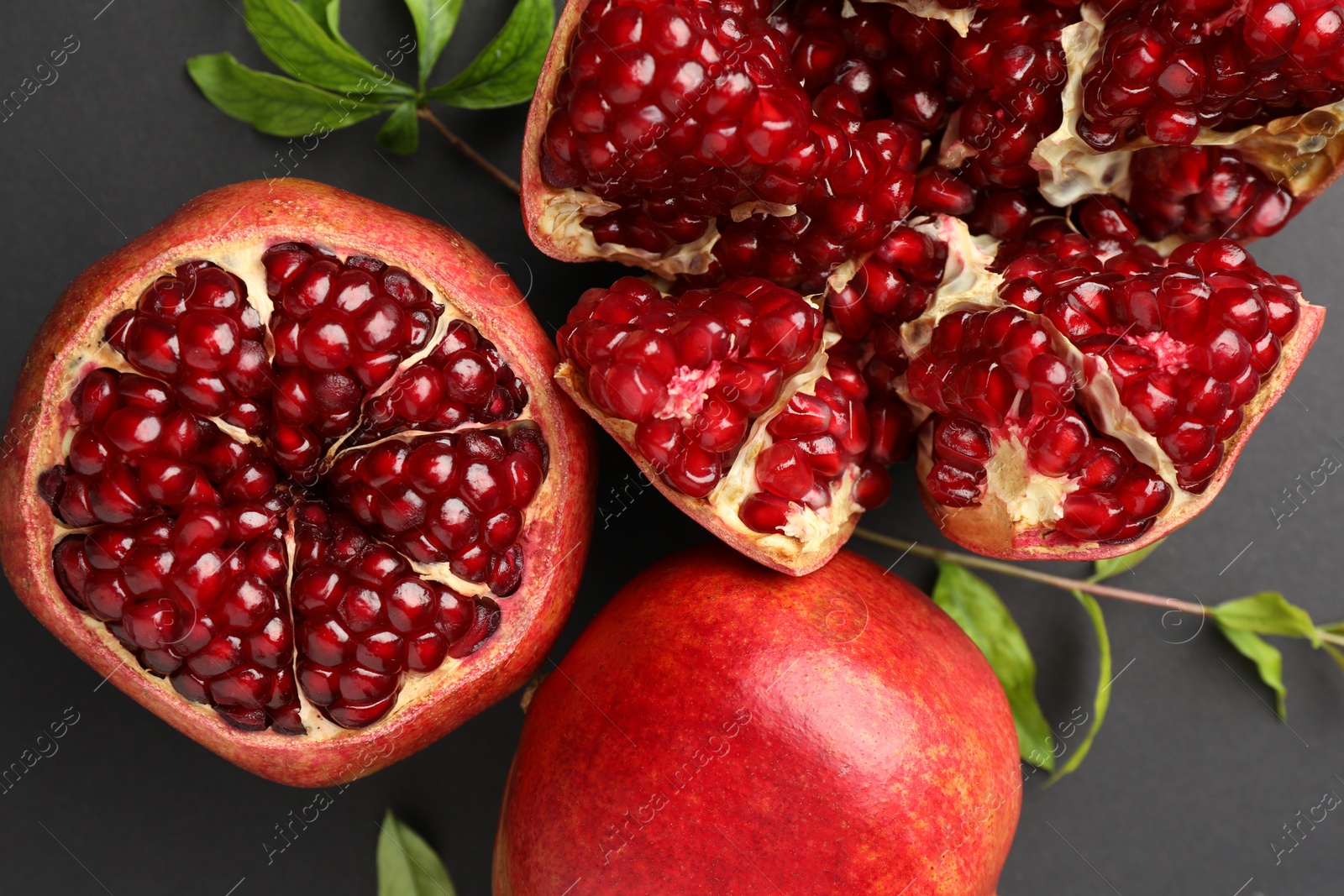 Photo of Fresh ripe pomegranates and leaves on grey background, top view