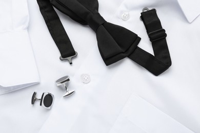 Photo of Stylish black bow tie and cufflinks on white shirt, top view