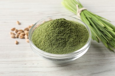 Photo of Wheat grass powder in glass bowl on white wooden table, closeup