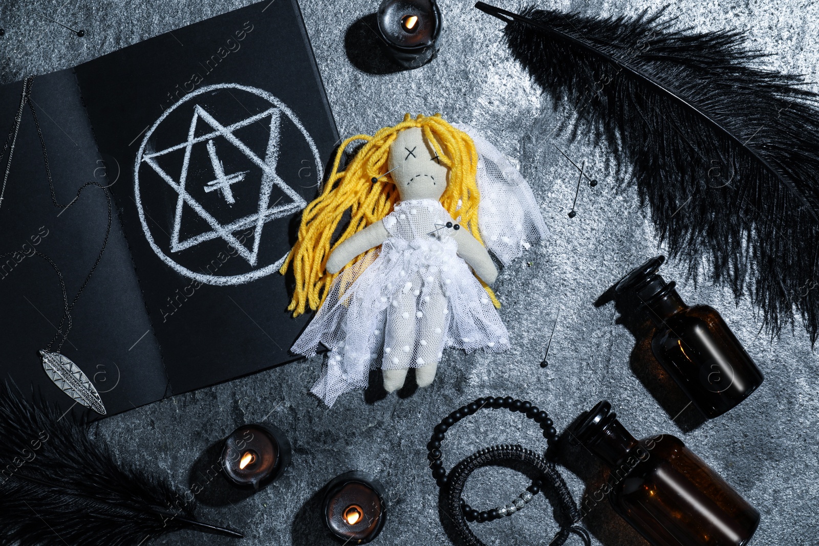Photo of Bride voodoo doll with pins surrounded by ceremonial items on grey table, flat lay