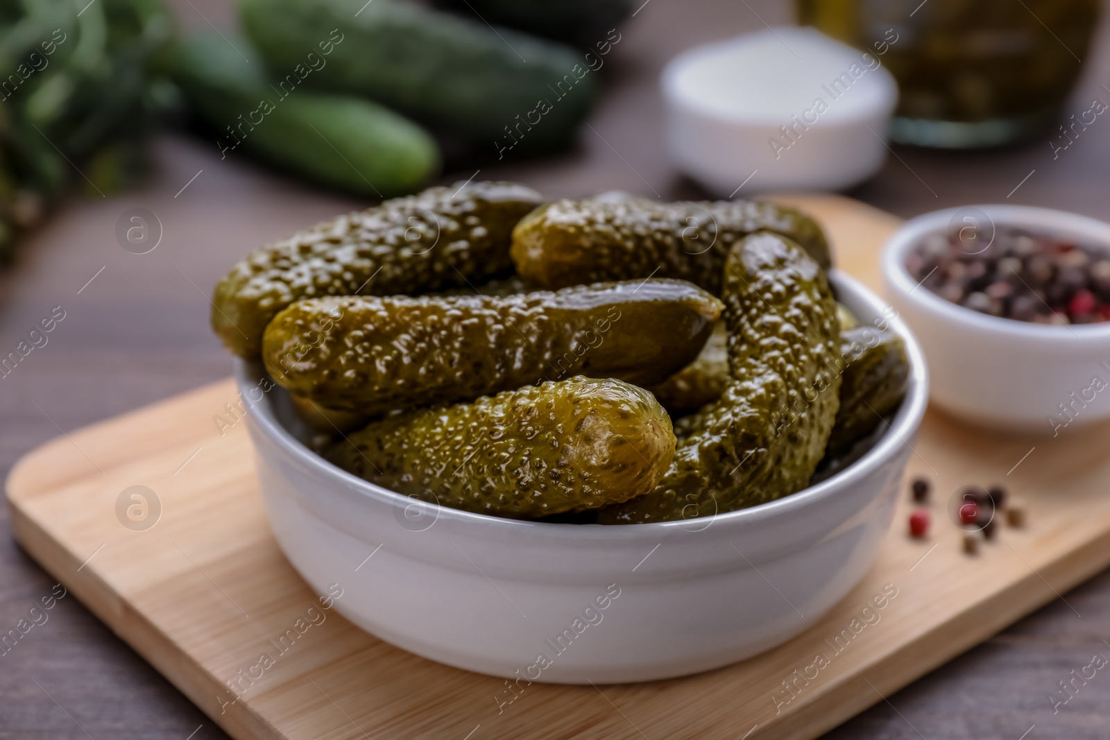 Photo of Bowl of pickled cucumbers and ingredients for food preservation on wooden table, closeup