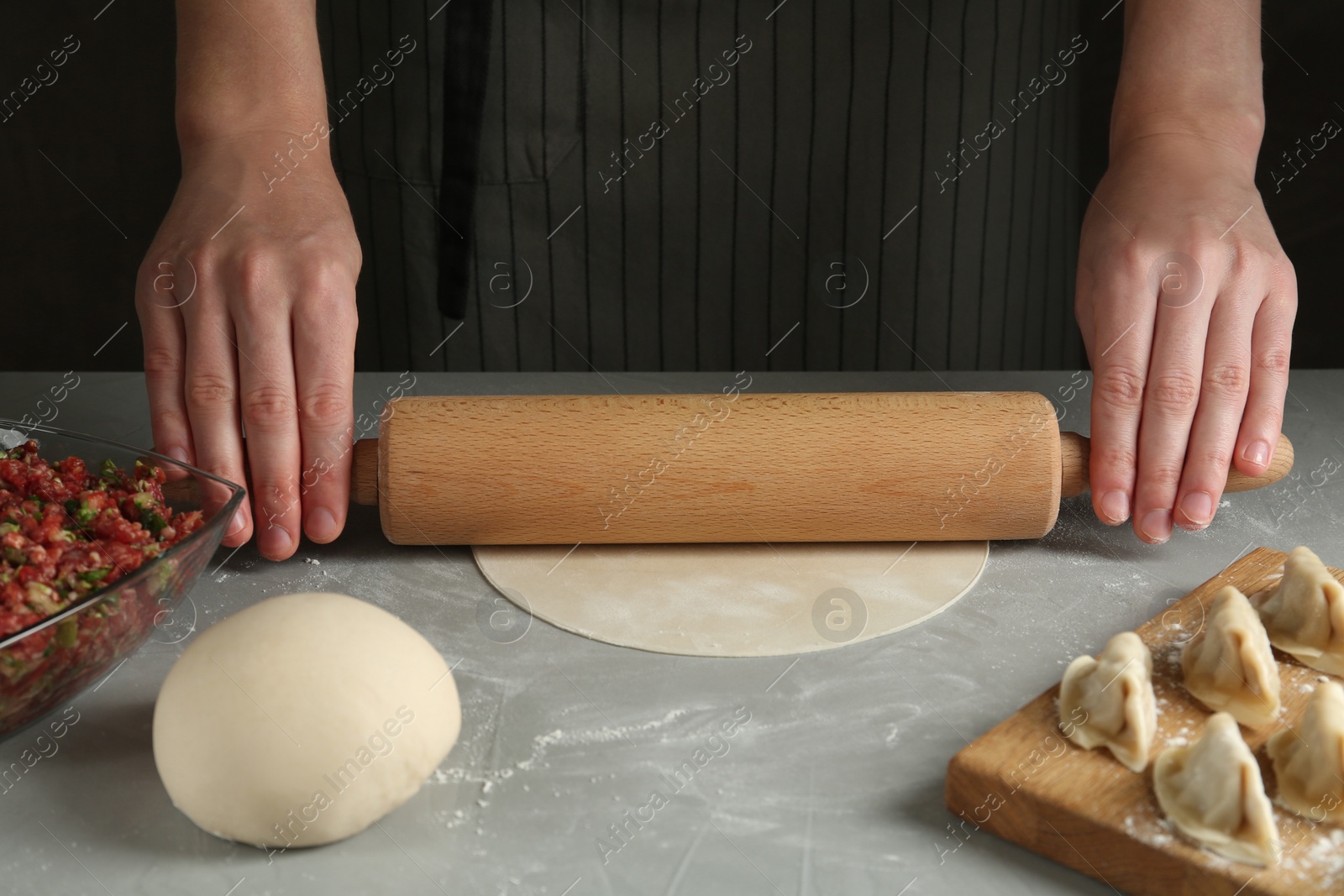 Photo of Woman rolling dough for gyoza at grey table, closeup