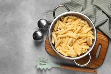 Photo of Delicious penne pasta in colander, spices and spoon on gray table, flat lay. Space for text