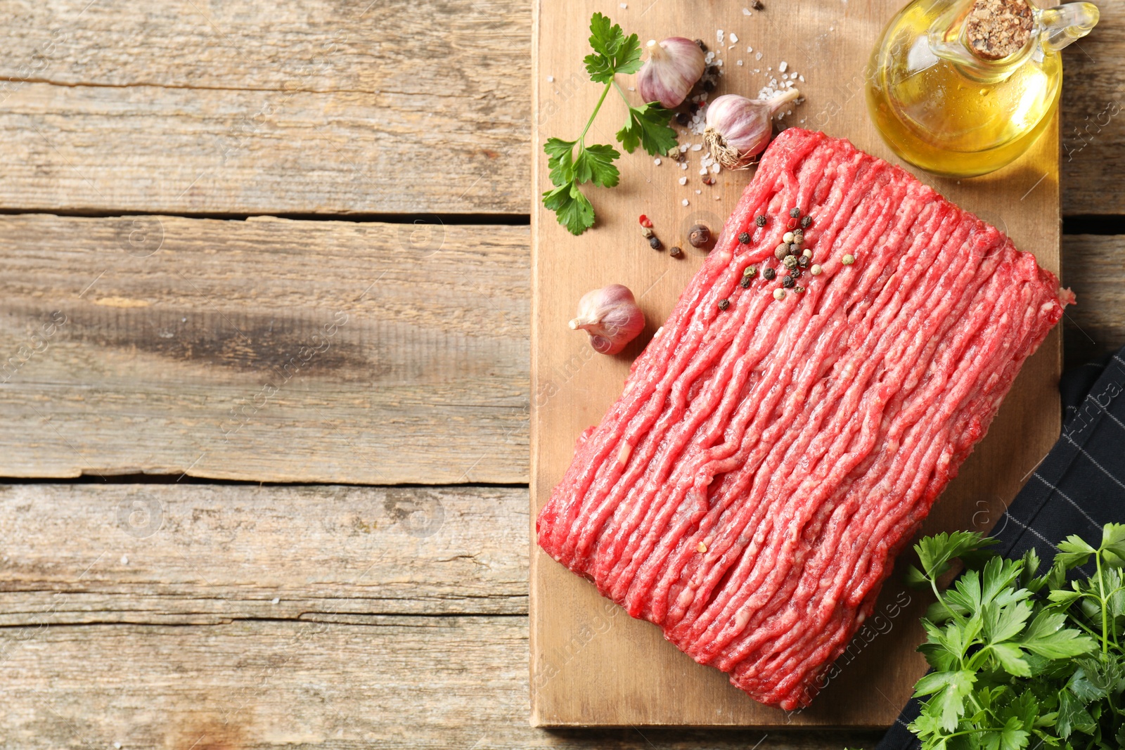 Photo of Raw ground meat, spices, parsley and oil on wooden table, top view. Space for text