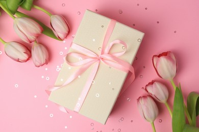 Photo of Beautiful gift box with bow, tulips and confetti on pink background, flat lay