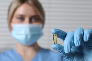 Doctor holding pill on light background, selective focus. Space for text