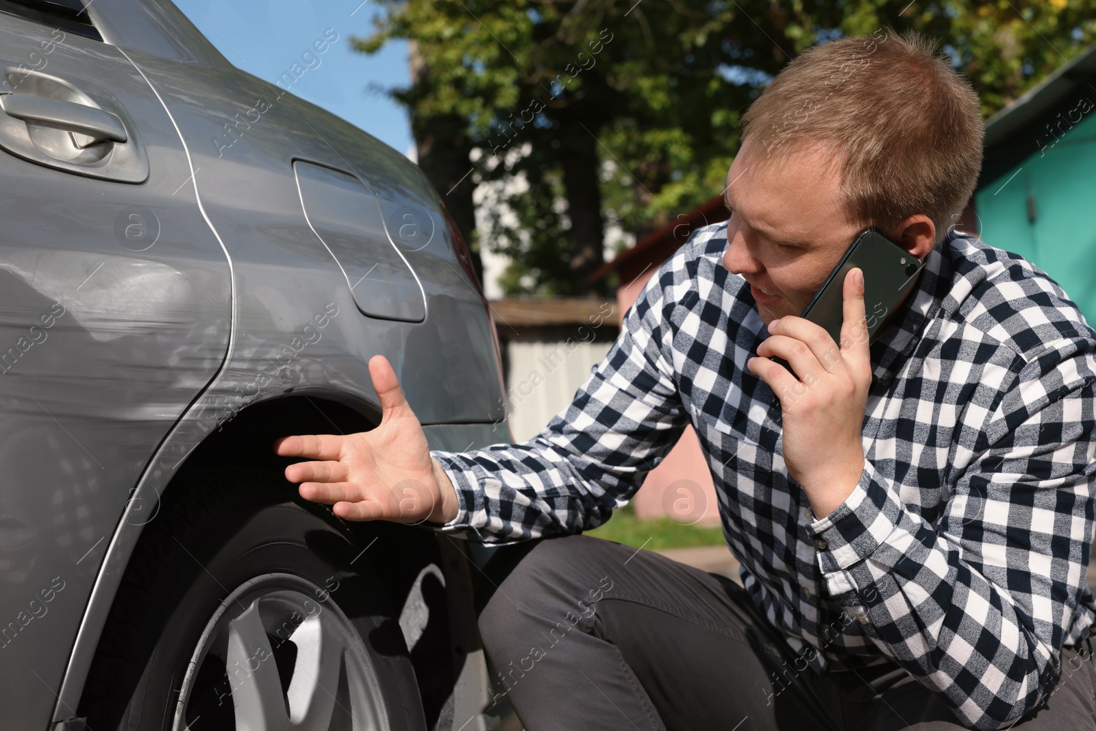 Photo of Man talking on phone near car with scratch outdoors