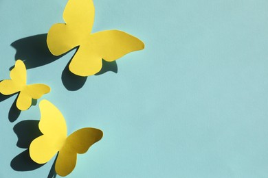 Photo of Yellow paper butterflies on turquoise background, top view. Space for text