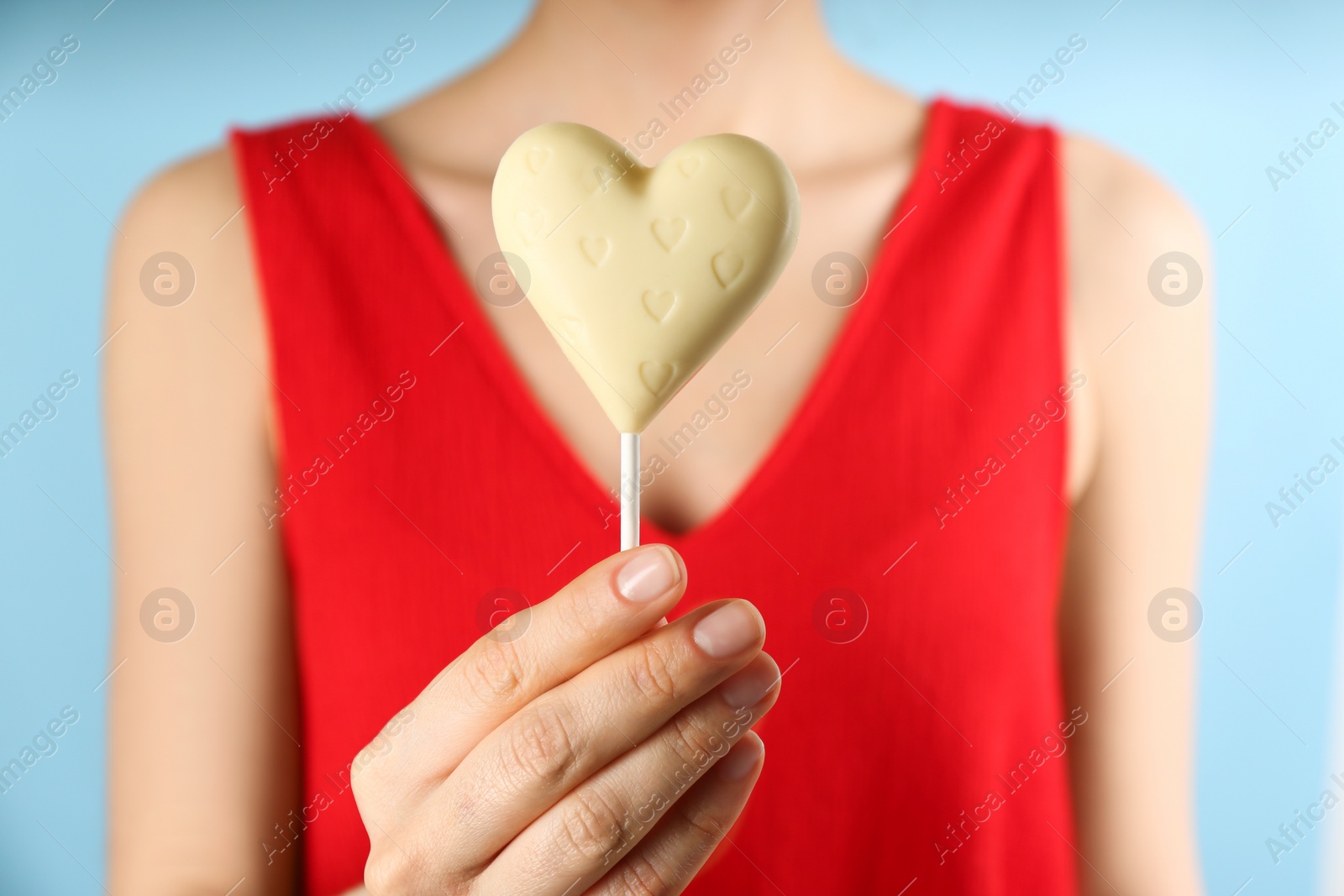 Photo of Woman holding heart shaped lollipop made of chocolate on light blue background, closeup