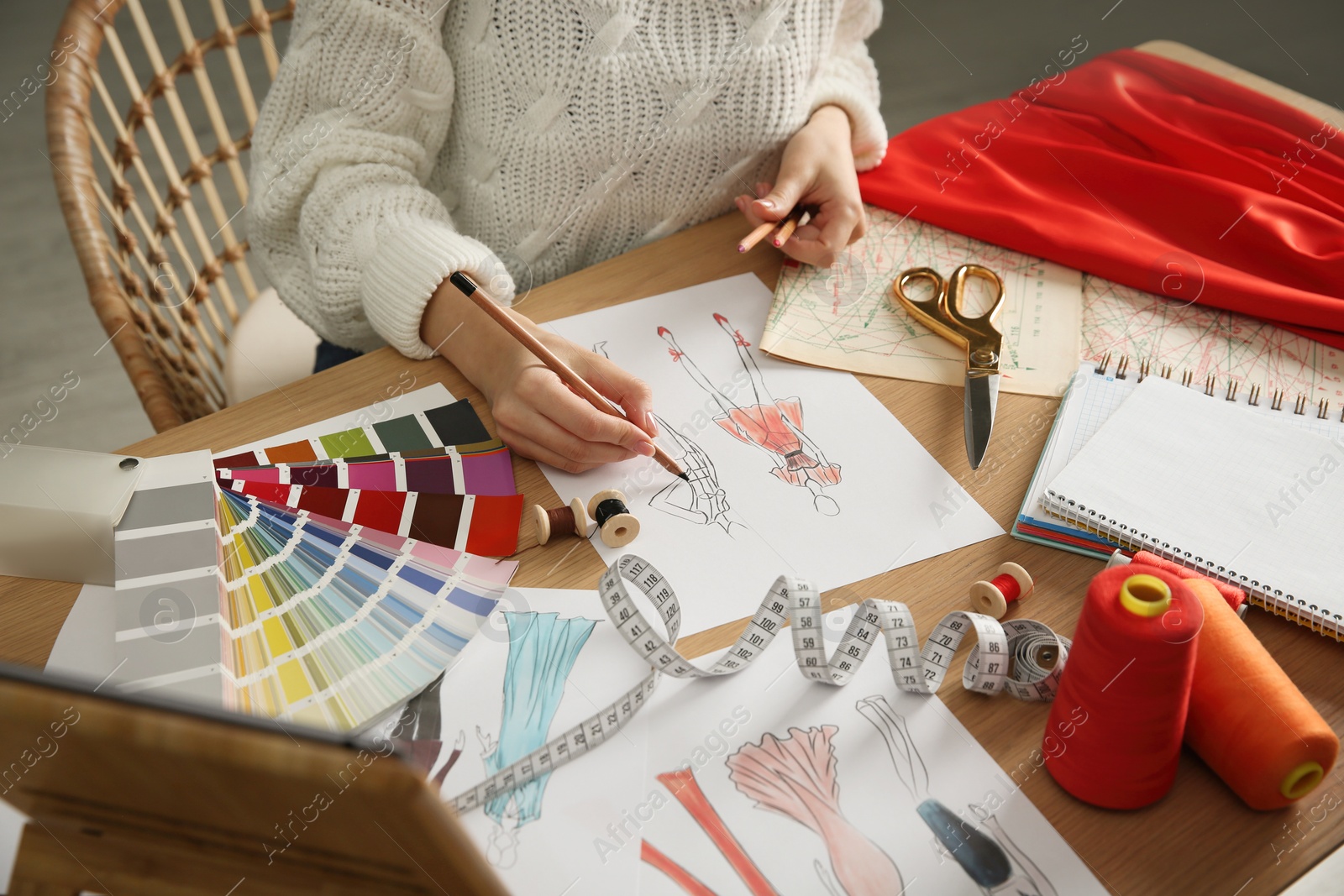 Photo of Fashion designer creating new clothes in sketchbook at wooden table indoors, closeup