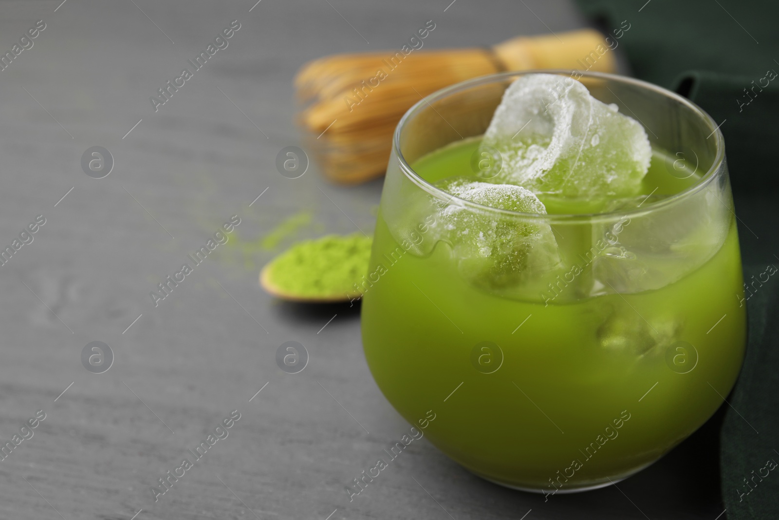 Photo of Glass of delicious iced green matcha tea on grey wooden table, closeup. Space for text