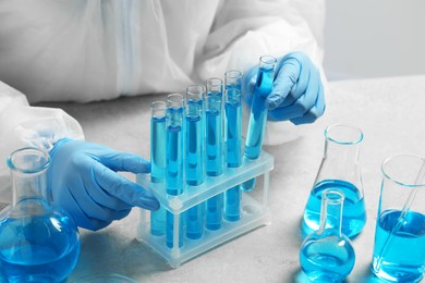 Scientist taking test tube with light blue liquid at white table in laboratory, closeup