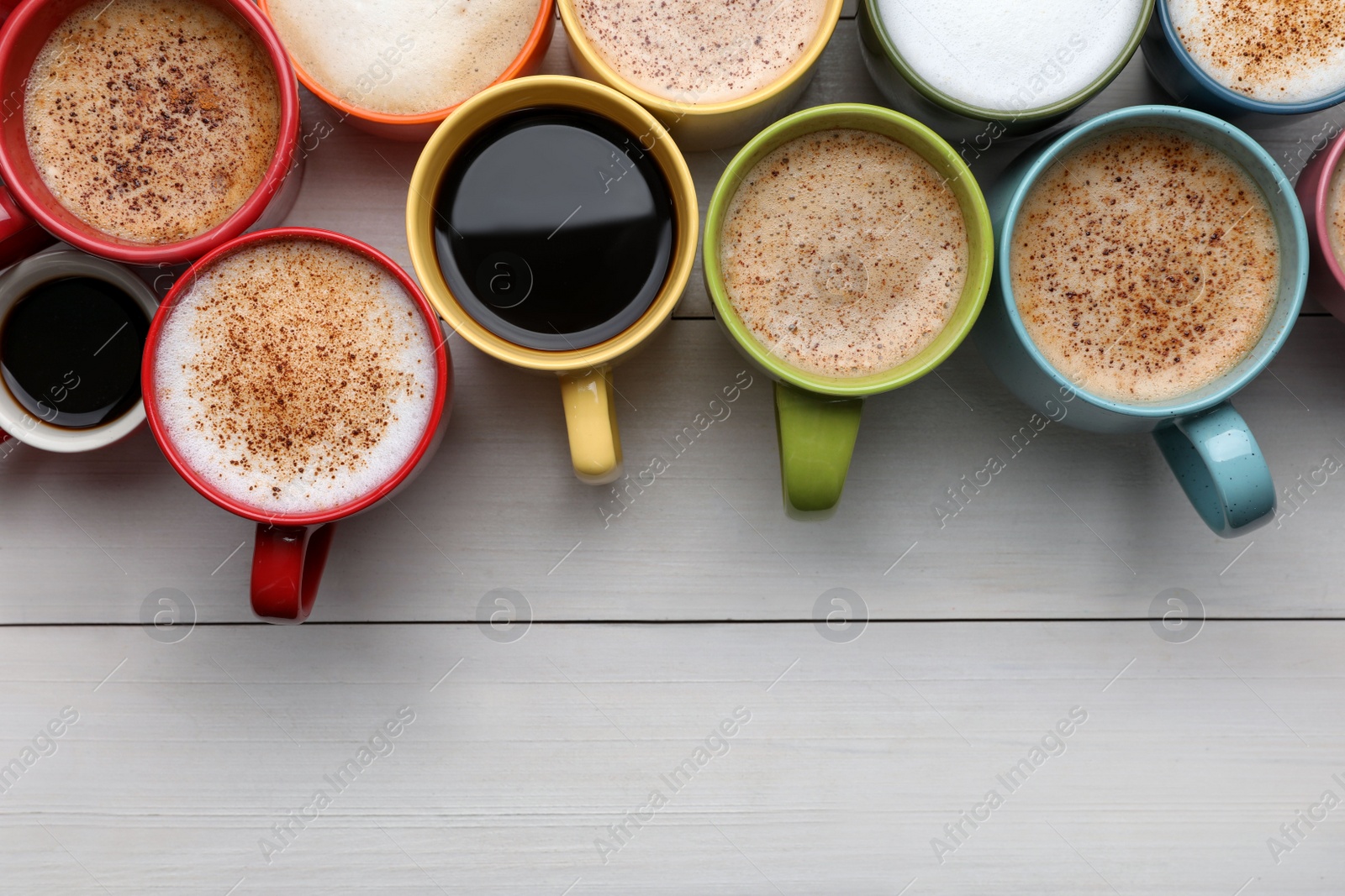 Photo of Many different cups with aromatic hot coffee on white wooden table, flat lay. Space for text