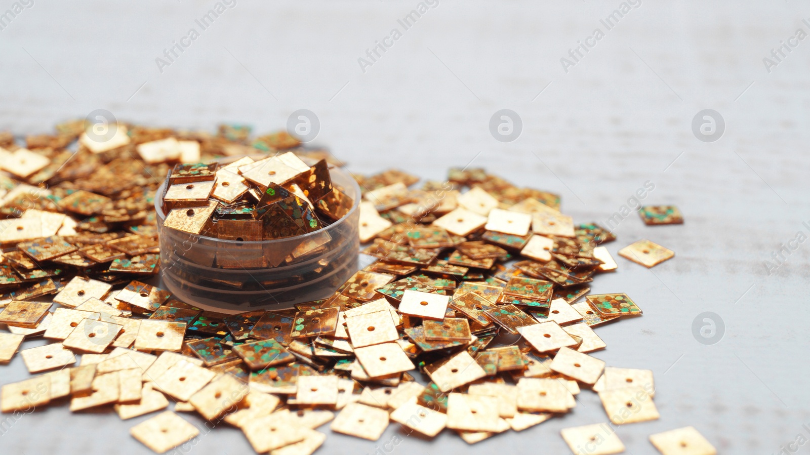 Photo of Pile of many golden sequins on white wooden table, closeup. Space for text