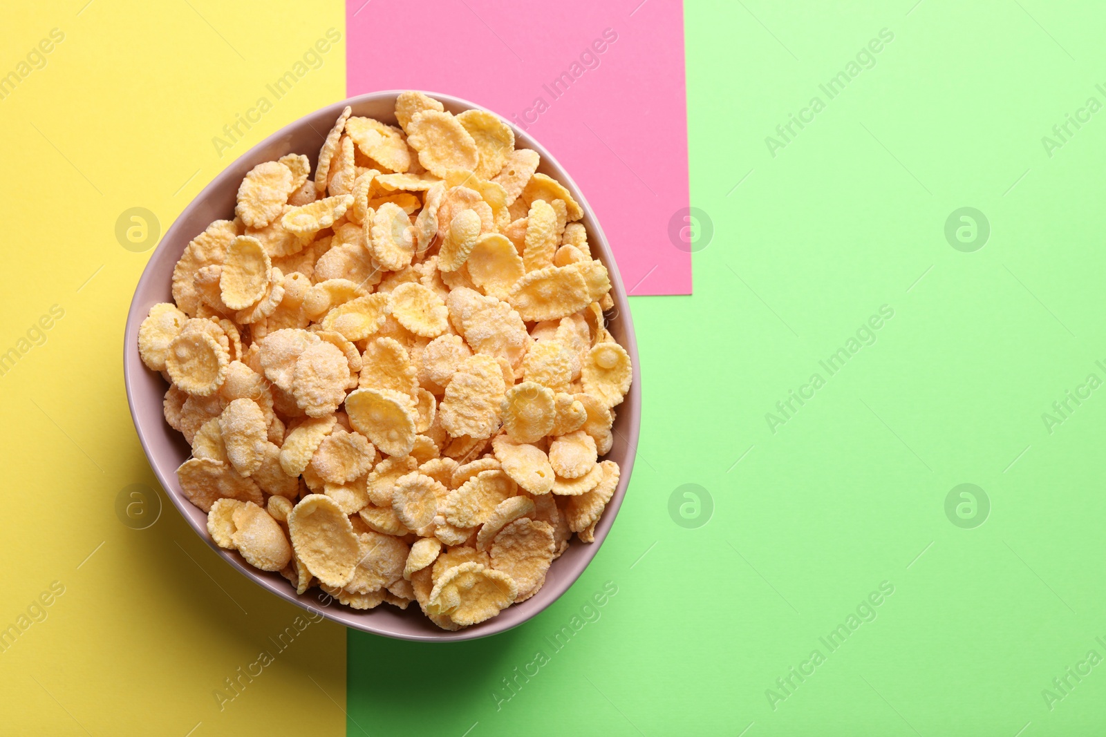 Photo of Bowl of tasty crispy corn flakes on color background, top view. Space for text