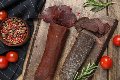Photo of Delicious dry-cured beef basturma with rosemary and tomatoes on wooden table, flat lay