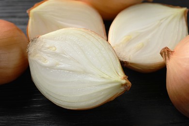 Whole and cut onions on black wooden table, closeup