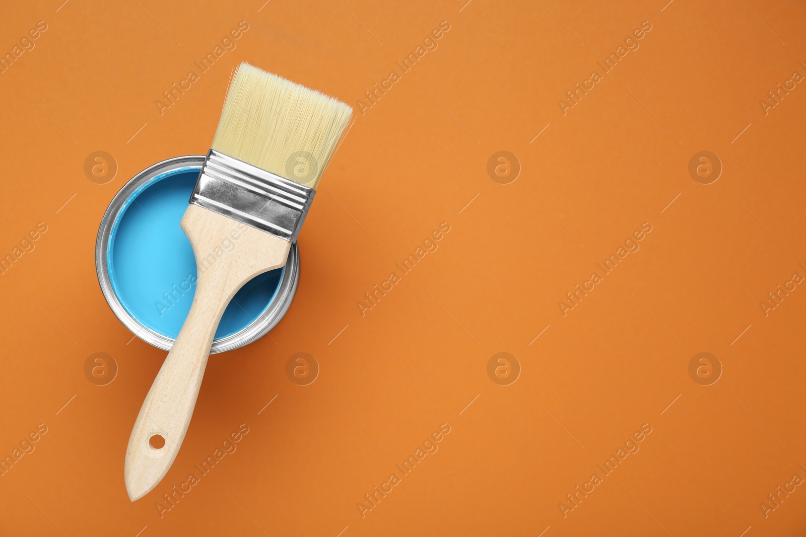 Photo of Can of light blue paint with brush on pale orange background, top view. Space for text