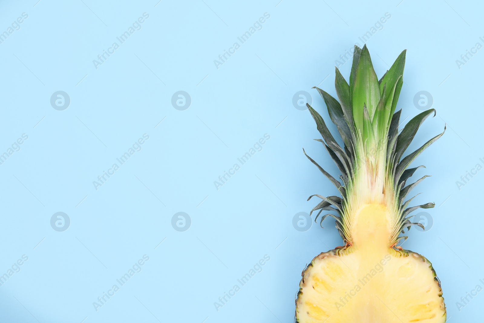 Photo of Half of ripe pineapple on light blue background, top view. Space for text