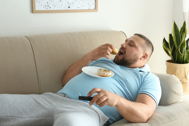 Photo of Lazy overweight man with donuts watching TV on sofa at home
