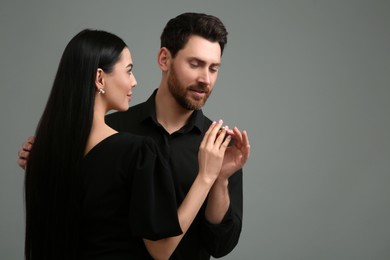 Photo of Man putting elegant ring on woman's finger against dark grey background. Space for text