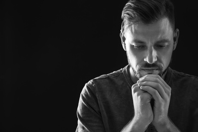 Photo of Man with hands clasped together for prayer on dark background, black and white effect. Space for text