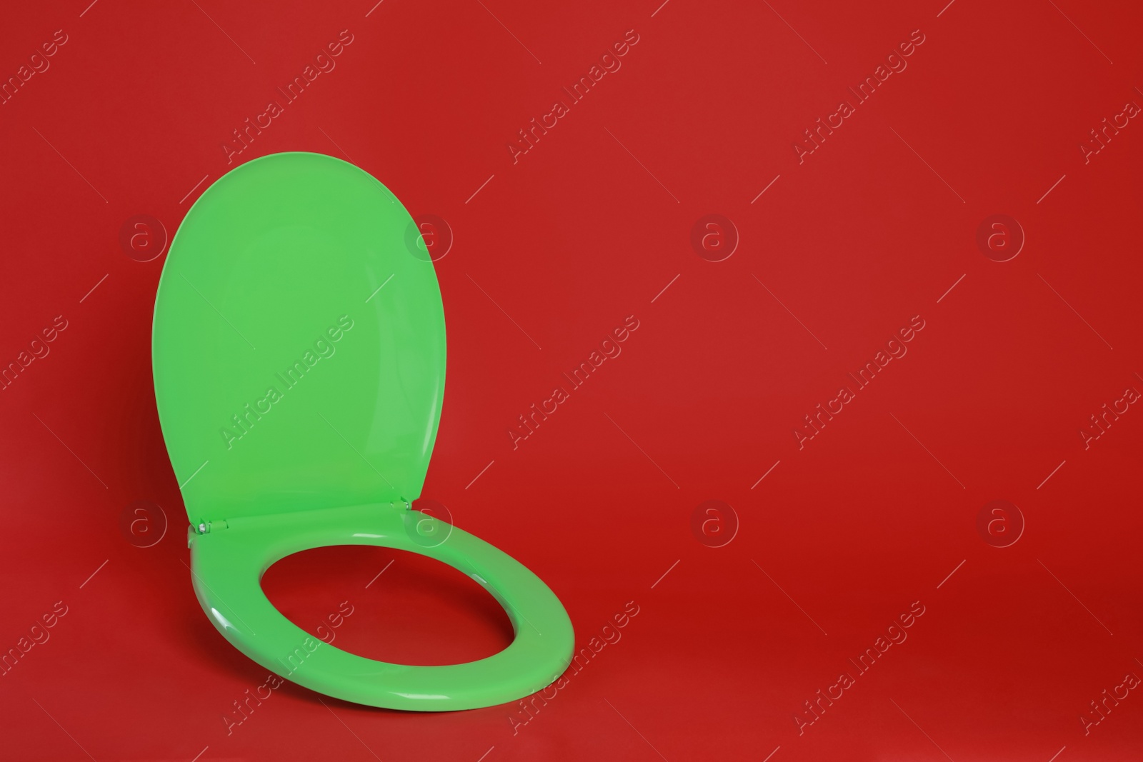 Photo of New green plastic toilet seat on red background, space for text