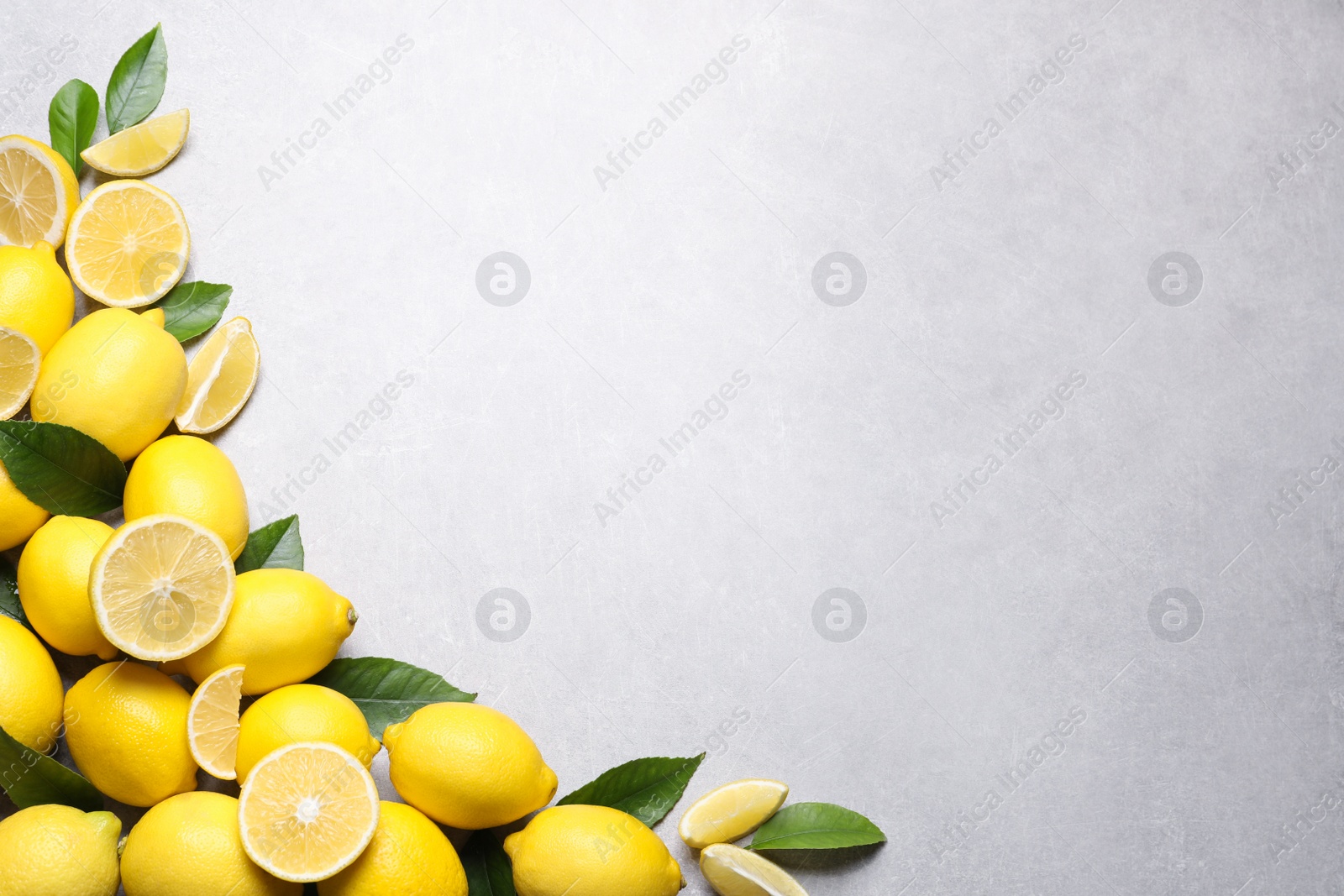 Photo of Many fresh ripe lemons with green leaves on light grey table, flat lay. Space for text