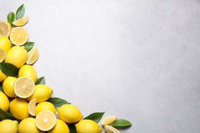 Photo of Many fresh ripe lemons with green leaves on light grey table, flat lay. Space for text