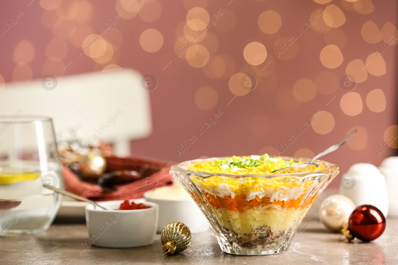 Photo of Traditional russian salad Mimosa and festive decor on table against blurred lights
