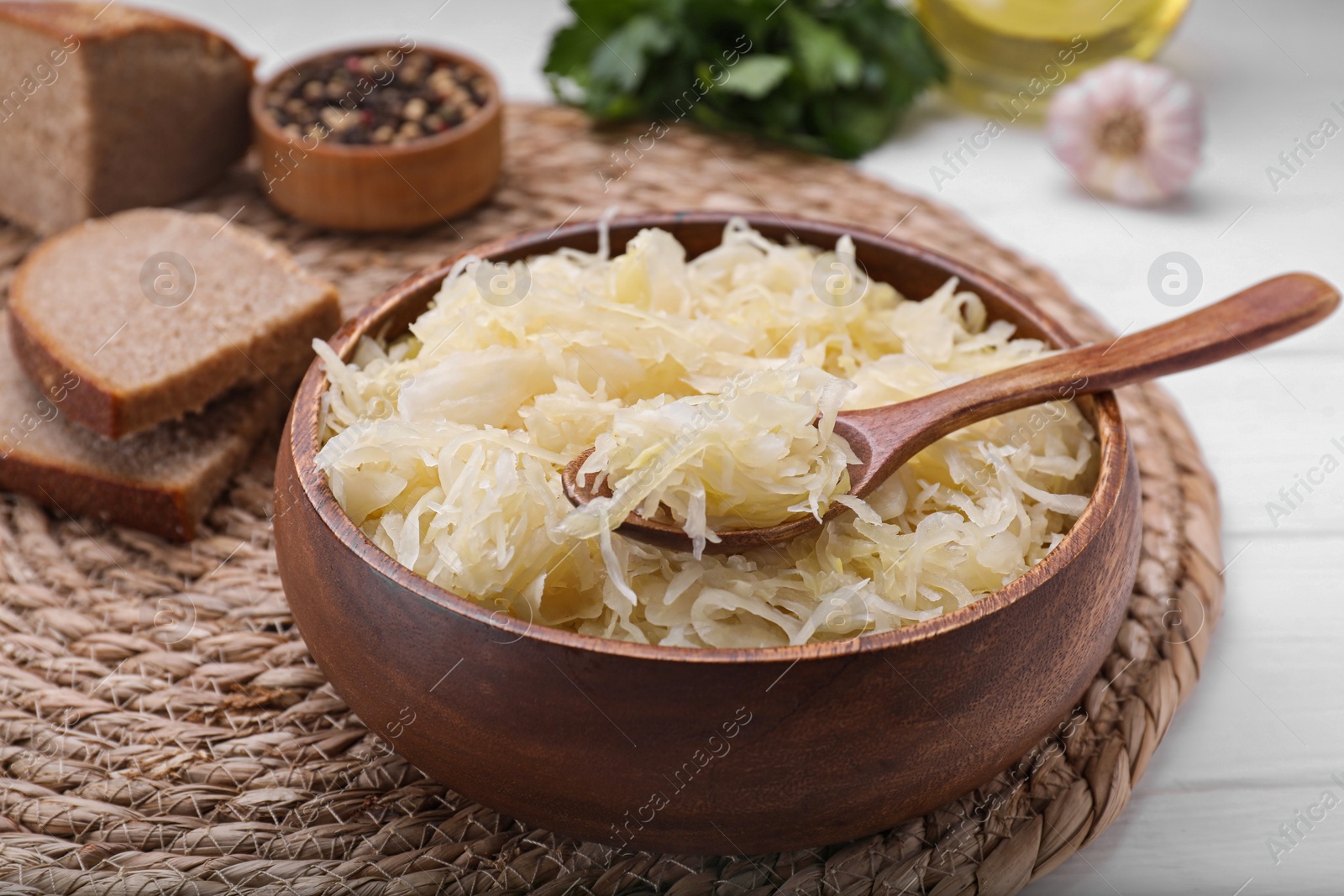 Photo of Bowl of tasty sauerkraut on white wooden table, closeup